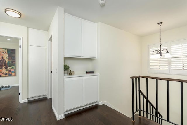 hall featuring an upstairs landing, a notable chandelier, baseboards, and dark wood-style flooring