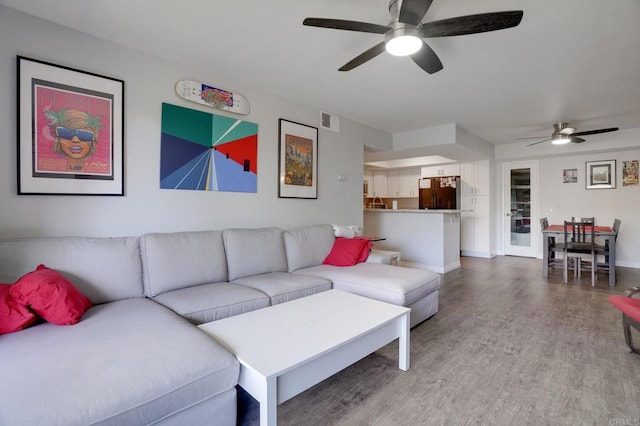 living room with light wood-type flooring, visible vents, baseboards, and a ceiling fan