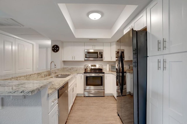 kitchen with visible vents, a tray ceiling, a sink, white cabinets, and appliances with stainless steel finishes