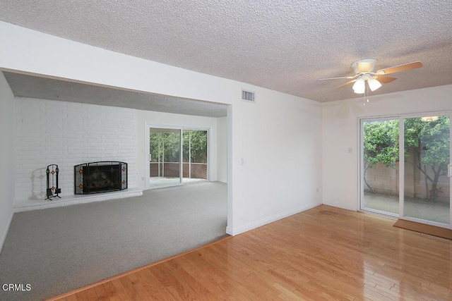 unfurnished living room with visible vents, a fireplace, wood finished floors, a textured ceiling, and a ceiling fan