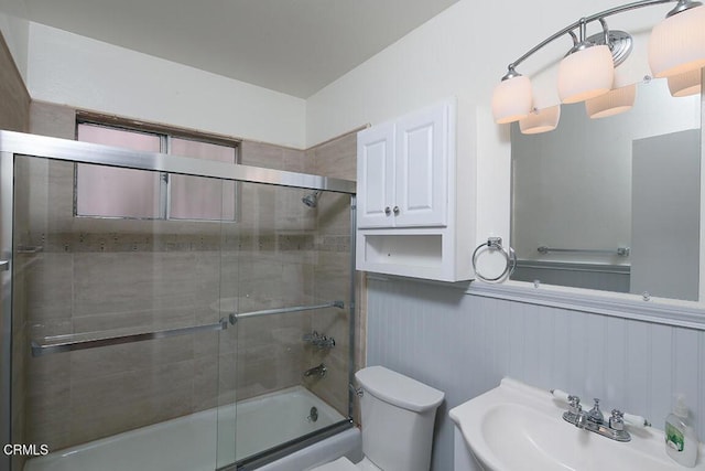 full bath with enclosed tub / shower combo, wainscoting, toilet, and a sink