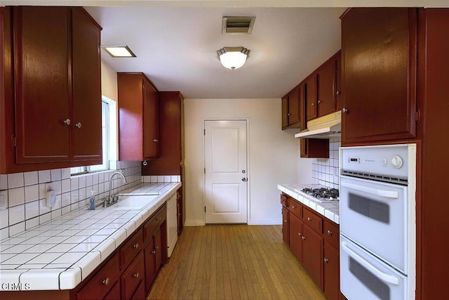 kitchen with under cabinet range hood, tile countertops, white appliances, and a sink