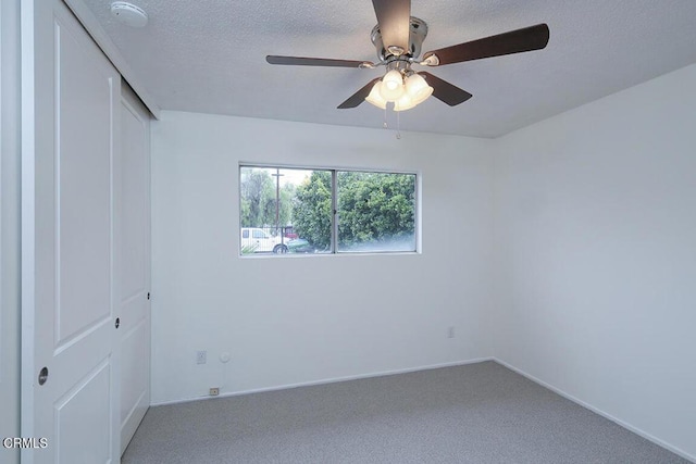 carpeted spare room with ceiling fan, baseboards, and a textured ceiling