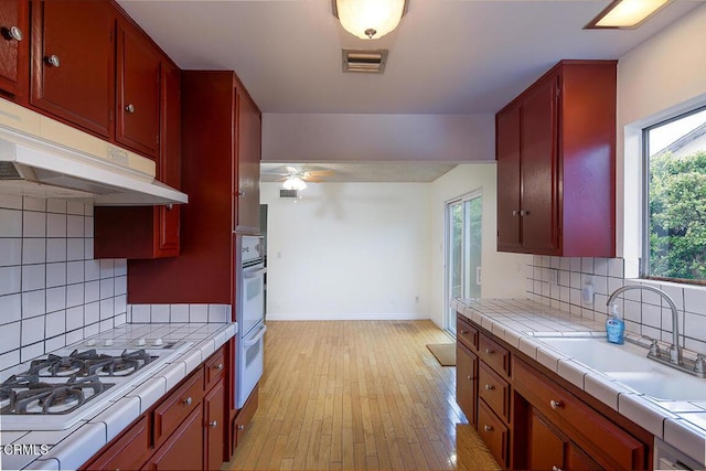 kitchen with tile countertops, white appliances, under cabinet range hood, and a sink