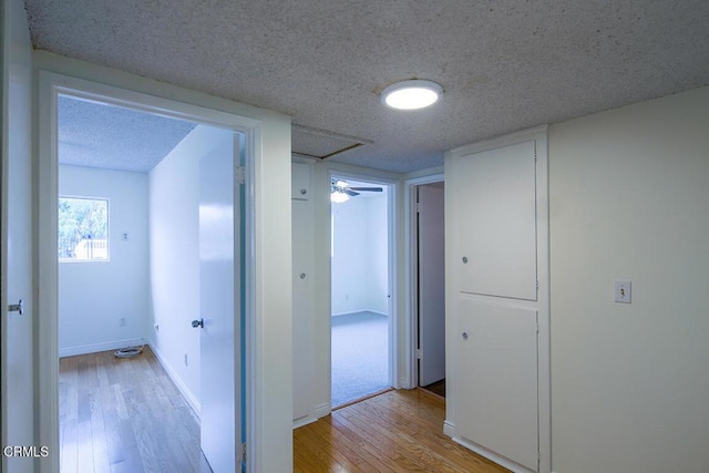 corridor with light wood-style flooring, baseboards, and a textured ceiling