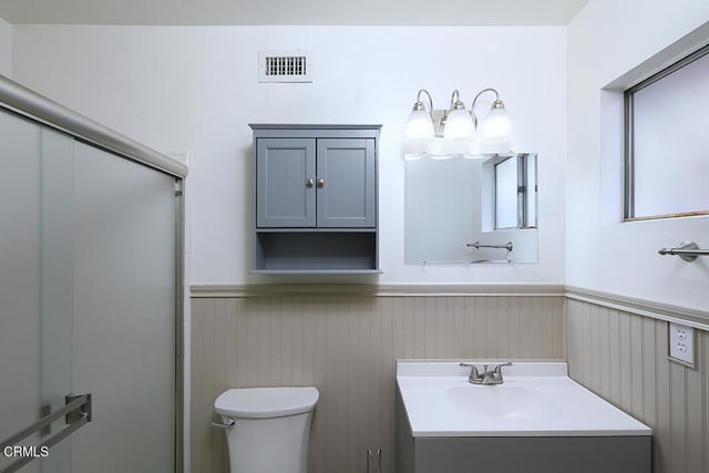 full bathroom featuring vanity, a shower with shower door, a wainscoted wall, toilet, and visible vents