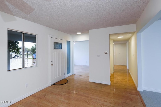 foyer entrance with a textured ceiling, light wood finished floors, and baseboards