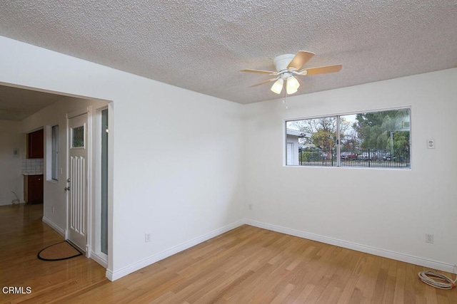 spare room featuring a textured ceiling, light wood finished floors, baseboards, and a ceiling fan