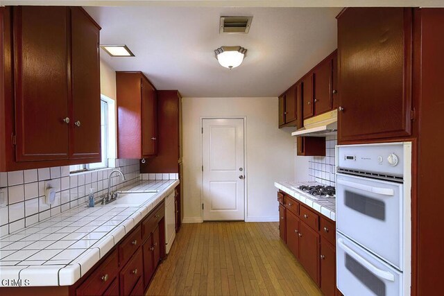 kitchen featuring tile countertops, under cabinet range hood, a sink, and white appliances