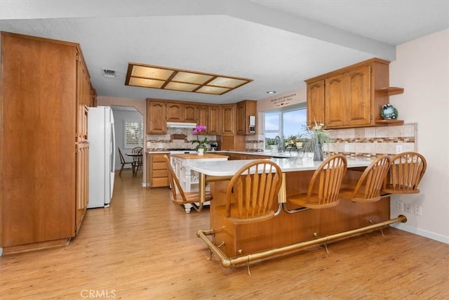 kitchen with brown cabinetry, visible vents, a peninsula, freestanding refrigerator, and under cabinet range hood