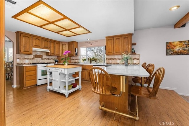 kitchen featuring brown cabinetry, open shelves, a peninsula, white range with gas cooktop, and under cabinet range hood