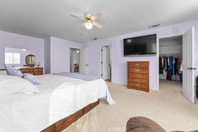 bedroom with a ceiling fan, visible vents, a closet, light carpet, and a walk in closet