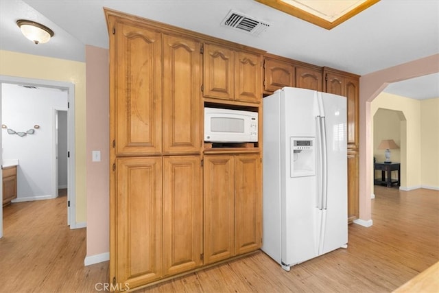 kitchen featuring visible vents, white appliances, arched walkways, brown cabinetry, and light wood finished floors