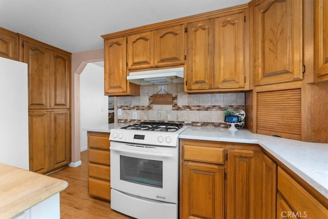 kitchen with under cabinet range hood, white appliances, brown cabinetry, and light countertops