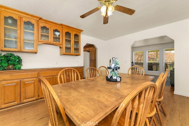 dining room featuring light wood-type flooring, arched walkways, a textured ceiling, and ceiling fan