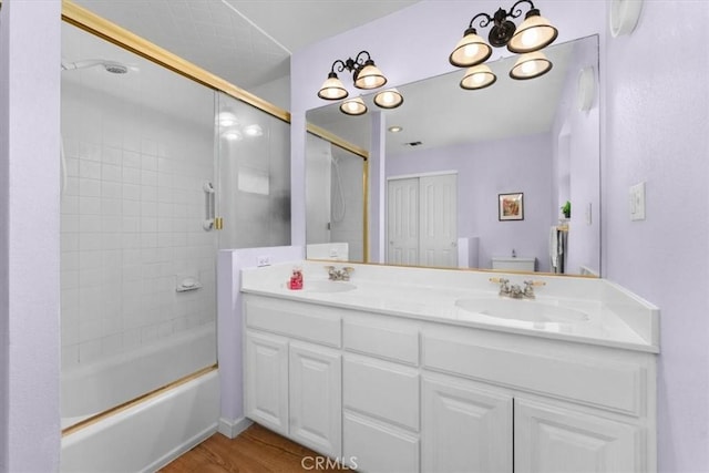 bathroom with a sink, combined bath / shower with glass door, wood finished floors, and double vanity