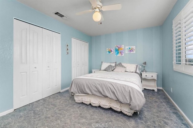 carpeted bedroom featuring visible vents, baseboards, two closets, and a ceiling fan