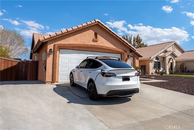 view of front of home with fence, a tiled roof, stucco siding, a garage, and driveway