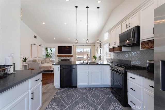 kitchen with dark countertops, a peninsula, white cabinets, black appliances, and a sink