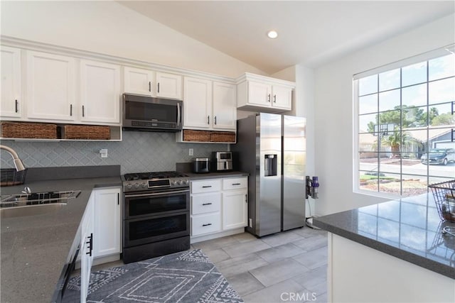 kitchen with lofted ceiling, a sink, appliances with stainless steel finishes, white cabinetry, and dark countertops