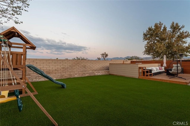 yard at dusk featuring a playground and a fenced backyard