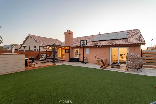 rear view of property featuring a patio area, roof mounted solar panels, and a tile roof