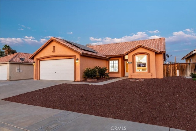 view of front of property with a tiled roof, roof mounted solar panels, stucco siding, a garage, and driveway