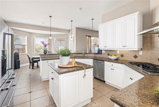 kitchen with a peninsula, a sink, appliances with stainless steel finishes, wall chimney exhaust hood, and tasteful backsplash