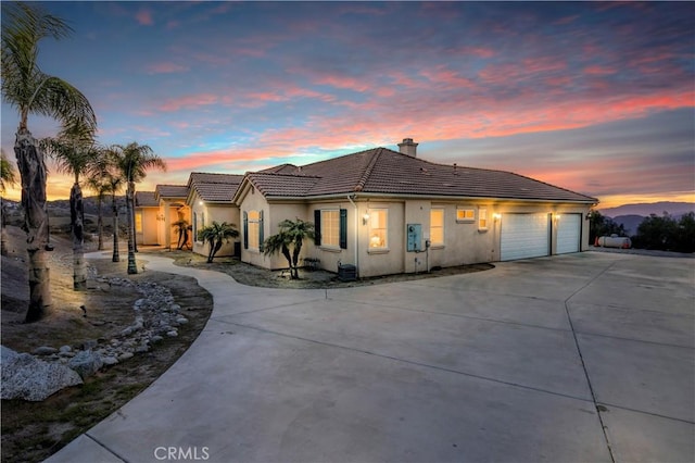 view of front of house with driveway, an attached garage, a chimney, stucco siding, and a tiled roof