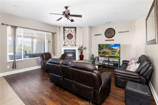 living room featuring a glass covered fireplace, baseboards, wood finished floors, and ceiling fan