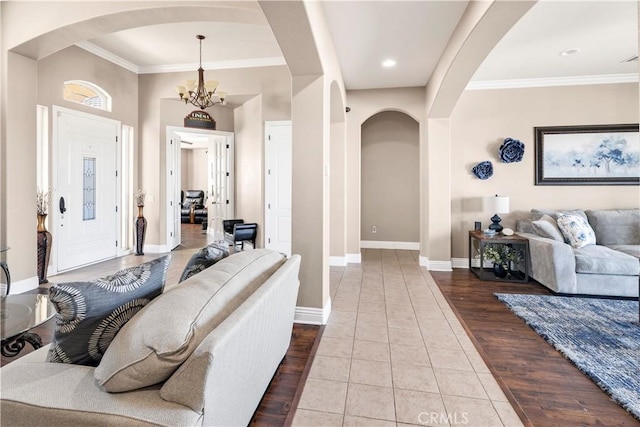 living room with wood finished floors, arched walkways, crown molding, baseboards, and a chandelier