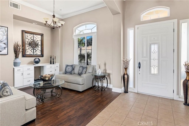 foyer with visible vents, ornamental molding, wood finished floors, an inviting chandelier, and baseboards