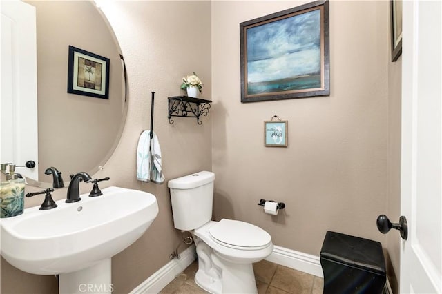 half bath featuring tile patterned floors, toilet, baseboards, and a sink