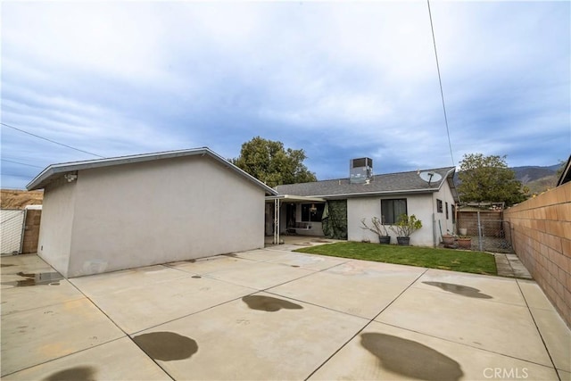 rear view of house with stucco siding, a patio, a lawn, and fence