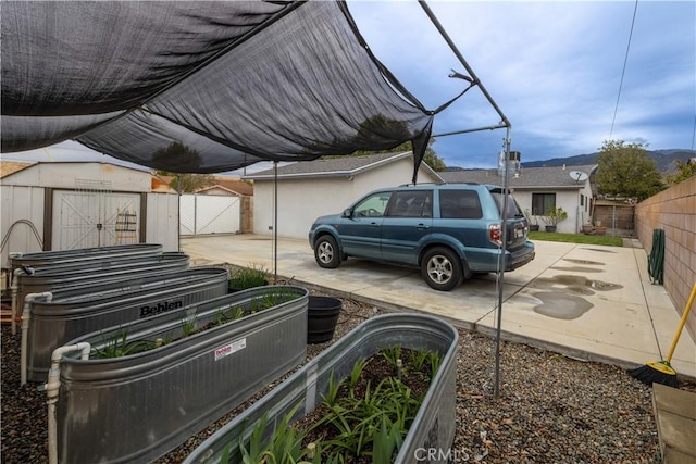 view of parking with a garden, a storage unit, and fence