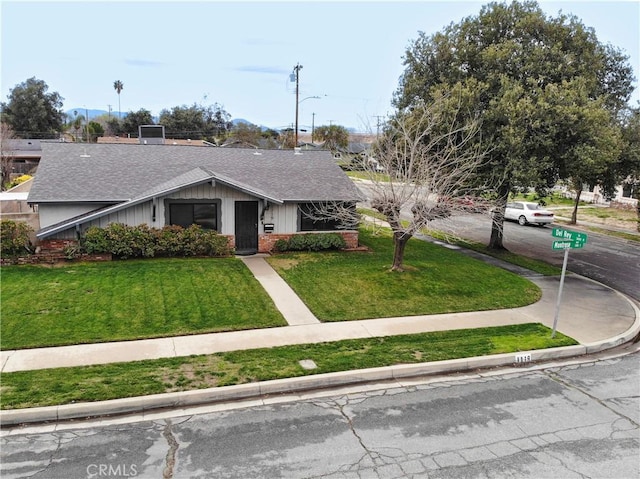 view of front of property with brick siding, a front yard, and roof with shingles