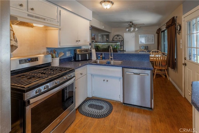 kitchen featuring under cabinet range hood, appliances with stainless steel finishes, a peninsula, white cabinets, and a sink