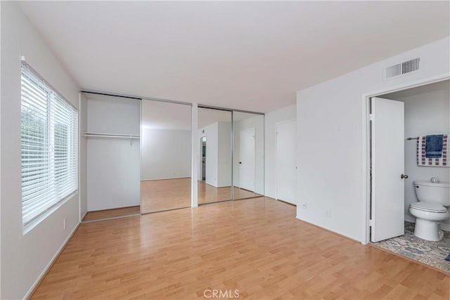 unfurnished bedroom with visible vents, multiple closets, light wood-style floors, and connected bathroom