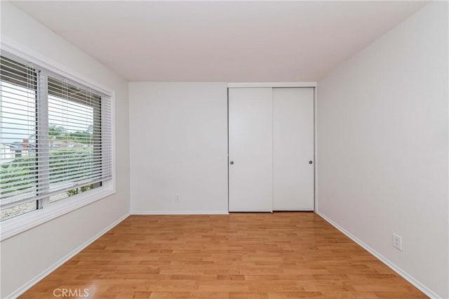 unfurnished bedroom featuring light wood-style flooring, baseboards, and a closet