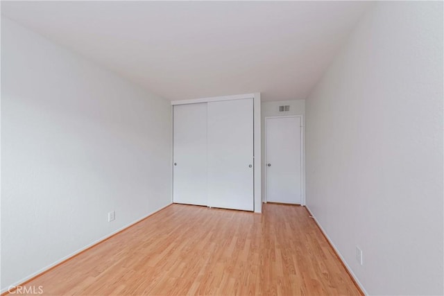 unfurnished bedroom featuring light wood-type flooring, visible vents, and a closet