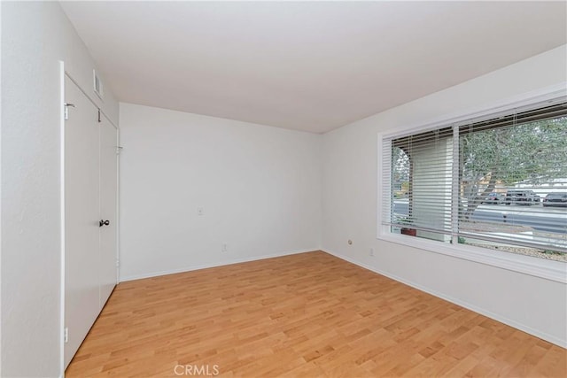 unfurnished room featuring light wood-style floors, visible vents, and baseboards