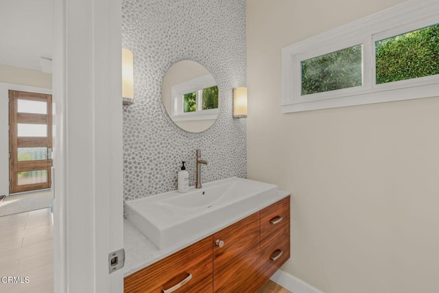 bathroom with wallpapered walls, vanity, baseboards, and an accent wall