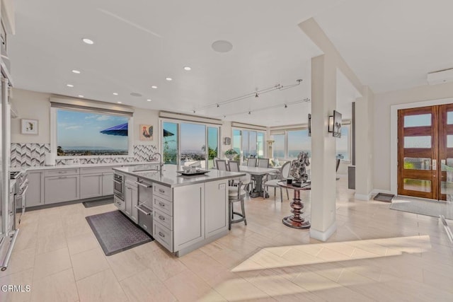 kitchen with gray cabinetry, a kitchen island with sink, a breakfast bar, a sink, and backsplash