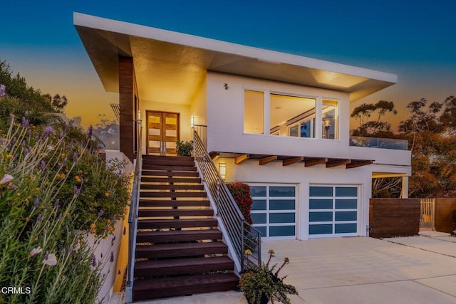 modern home with driveway, an attached garage, stairway, and stucco siding