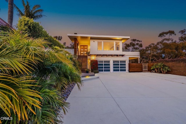 view of front of property featuring concrete driveway, stucco siding, fence, stairway, and a garage
