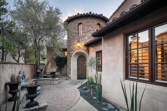 doorway to property featuring stucco siding, stone siding, a patio, and fence