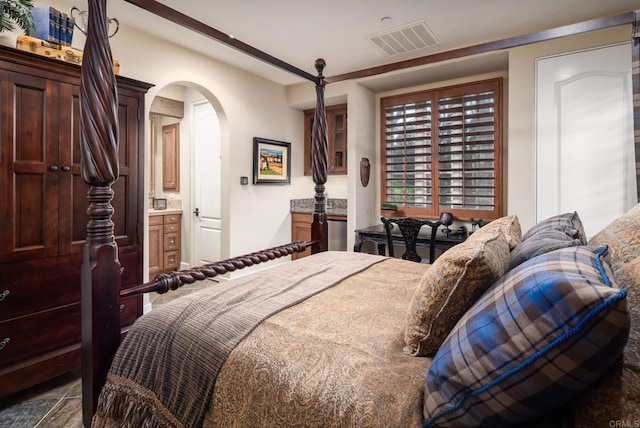 bedroom featuring arched walkways, visible vents, and ensuite bath