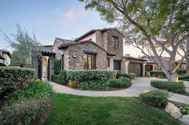 mediterranean / spanish-style home with a tile roof, stone siding, a front yard, and stucco siding