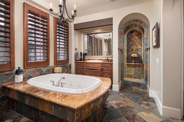 full bath with vanity, stone tile floors, a tub with jets, tiled shower, and a notable chandelier