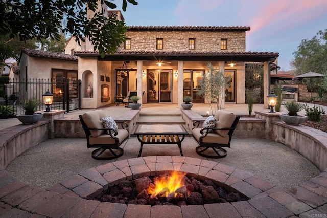 back of house with stucco siding, a tiled roof, fence, a fire pit, and a patio area